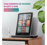 El Kindle 2024 11va Gen de 6" con funda transparente DIETEC y mica se muestra en un soporte de carga inalámbrica, junto a un vaso de agua y una planta. Texto: Carga sin quitar la funda transparente protectora.